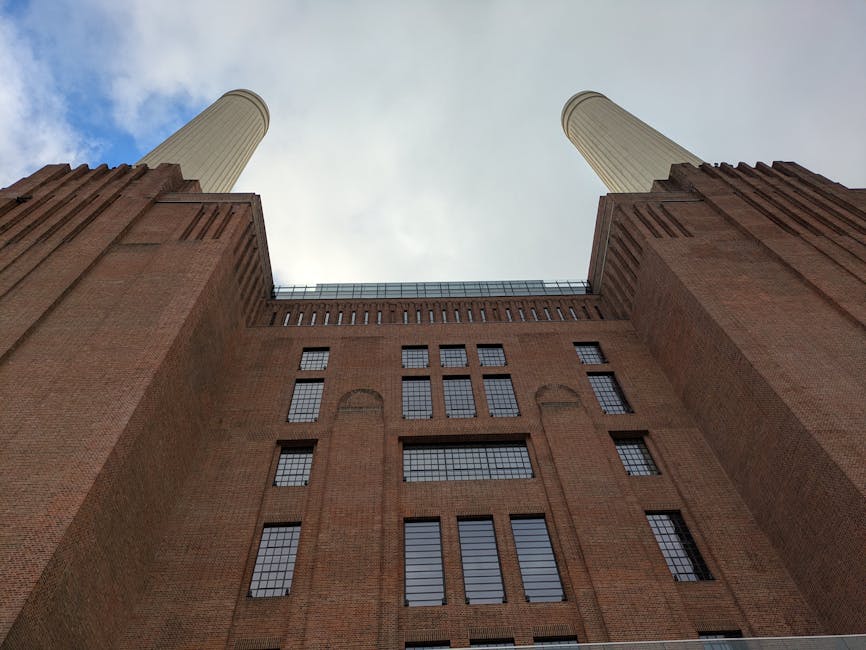 The image shows the historic Battersea Power Station situated by the River Thames at sunset, with a vibrant pink and purple sky overhead. The building is constructed from red brick and features four t